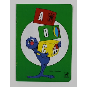 May include: A vintage children's book cover featuring a blue, furry character holding alphabet blocks. The blocks are red, green, and yellow, with the letters A, B, and C. The background is green with a white circle.