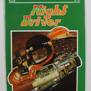 Könnte beinhalten: Eine grüne Atari-Spielbox mit dem Titel "Night Driver" in orange, grün und roten Buchstaben. Die Box zeigt ein Nahaufnahmebild eines Rennfahrers mit Helm, der ein weißes Rennfahrzeug fährt.