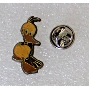 May include: A yellow and brown cartoon bird pin with a black outline. The pin has a silver back with a safety clasp.