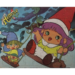 Puede incluir: Un rompecabezas vintage con una niña de dibujos animados con cabello morado que lleva un gorro de Papá Noel rojo, montando un columpio con dos figuras de dibujos animados más pequeñas. El rompecabezas se titula "Memule La Piccola" y tiene 50 piezas.