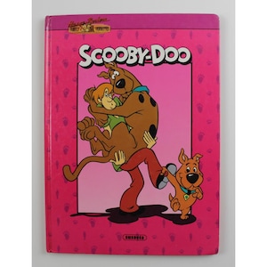 May include: A vintage Scooby-Doo book with a pink cover featuring the cartoon characters Scooby-Doo, Shaggy, and another puppy. The title "SCOOBY-DOO" is in white letters. The cover has a pink background with paw prints.