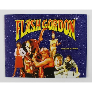 Puede incluir: Una portada de álbum de cromos vintage de Flash Gordon con un grupo de personajes de la película. La portada es de un azul vibrante con estrellas blancas y el título "FLASH GORDON" en letras amarillas, rojas y negras. El texto "COLECCION DE CROMOS" está en la esquina inferior derecha.