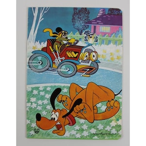 May include: A vintage Disney notebook cover featuring a cartoon scene. The top half shows a dog driving a red car, while the bottom half depicts Pluto lying on the ground. The background includes a house, trees, and a night sky.
