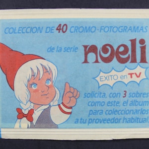 May include: A blue and white illustration of a girl with a red hat and white hair. The text reads "COLECCION DE 40 CROMO-FOTOGRAMAS de la serie noeli EXITO en TV solicita, con 3 sobres como este, el álbum para coleccionarlos a tu proveedor habitual."