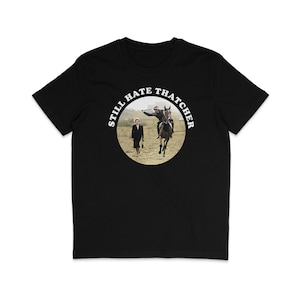 Puede incluir: Camiseta negra con un gráfico circular blanco que dice "Still Hate Thatcher" y una foto de Margaret Thatcher y un hombre a caballo.