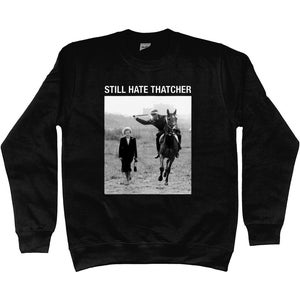 Puede incluir: Sudadera negra con estampado gráfico. El estampado presenta una imagen en blanco y negro de una persona caminando y una persona a caballo. El texto "STILL HATE THATCHER" está encima de la imagen.