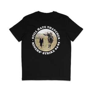 Puede incluir: Camiseta negra con un gráfico circular blanco que dice "Still Hate Thatcher. Miners' Strike '84-'85" y una foto de Margaret Thatcher montando a caballo.