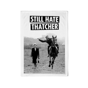 Puede incluir: Fotografía en blanco y negro de una mujer que se aleja de la cámara mientras una persona a caballo cabalga hacia la cámara. El texto "STILL HATE THATCHER" está impreso en letras negras en negrita en la parte superior de la imagen.