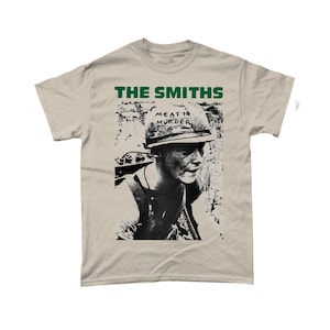 May include: A beige t-shirt with a black and white image of a person wearing a helmet with the words "Meat is Murder" written on it. The text "The Smiths" is printed in black above the image.