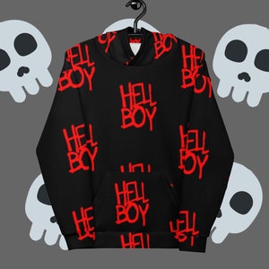 Puede incluir: Sudadera negra con un patrón rojo de "HELL BOY". La sudadera con capucha tiene un bolsillo delantero y una capucha. El diseño se repite en la tela. El fondo presenta gráficos de calaveras de dibujos animados.