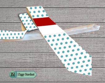 Op de afbeelding: Een stropdas met turquoise stippen op een witte achtergrond, met een rode streep. De stropdas ligt op een houten oppervlak, met de tekst "Ziggy Stardust".