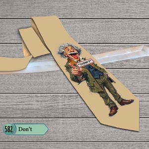 Può includere: Una cravatta color marrone chiaro con un'illustrazione grafica di un uomo dai capelli grigi spettinati, che indossa un abito verde e scarpe marroni, che punta in avanti con la bocca aperta. Un piccolo cartello rettangolare riporta il testo "DON'T".