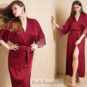 May include: A long, burgundy satin robe with lace trim on the sleeves. The robe has a tie belt and a front slit.