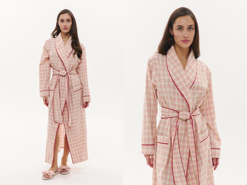 May include: A long, pink and cream plaid robe with red trim. The robe features a matching belt and pockets. The model is wearing matching pink bow slippers. The robe is designed for comfort and relaxation.