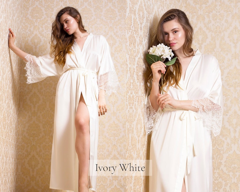 May include: A long white satin robe with lace trim on the sleeves. The robe is tied at the waist with a matching sash. The text "Ivory White" is visible at the bottom of the image.