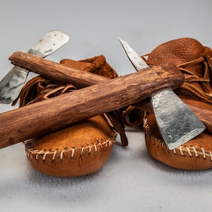 May include: Two small, brown leather moccasins with fringe and a wooden handle with two metal tomahawks attached.