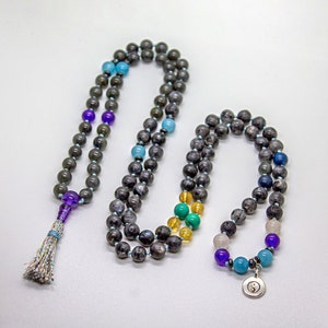 May include: A gray beaded necklace with a tassel and a yin yang charm. The necklace features various colored beads, including purple, blue, green, and yellow.