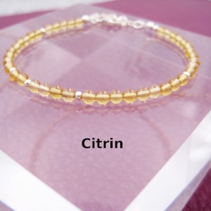 Könnte beinhalten: Ein Citrin-Armband mit silbernen Perlen und einem silbernen Verschluss. Das Armband liegt auf einer weißen Oberfläche.