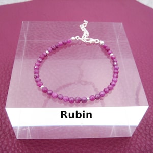 Könnte beinhalten: Ein zartes Armband mit kleinen, facettierten, runden, tiefrosa Rubinperlen. Das Armband hat silberfarbene Akzente und einen Kettenverschluss. Das Wort "Rubin" wird auf einem weißen Etikett angezeigt.