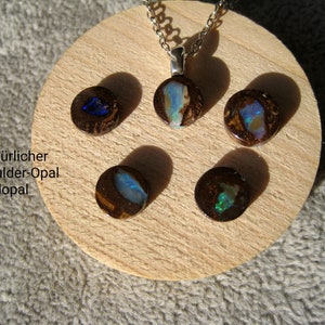 Könnte beinhalten: Fünf runde Boulder-Opal-Cabochons, einer an einer silbernen Kette, auf einer Holzoberfläche präsentiert. Die Opale sind braun mit blauen, grünen und weißen Schimmern.
