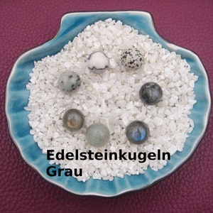 Könnte beinhalten: Eine blaue, muschelförmige Schale gefüllt mit weißem Kies und sechs grauen Edelsteinkugeln. Der Text "Edelsteinkugeln Grau" ist auf die Schale gedruckt.