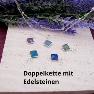 Könnte beinhalten: Eine doppelte Silberkette mit kleinen Metallperlen und fünf einzelnen quadratischen Edelsteinanhängern in Violett, Hellblau, Dunkelblau und Grün. Auf der Oberfläche ist der Text "Doppelkette mit Edelsteinen" aufgedruckt.