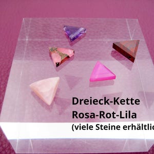 Puede incluir: Cinco gemas triangulares en rosa, morado y marrón sobre un bloque de acrílico transparente. El texto "Dreieck-Kette Rosa-Rot-Lila" es visible, lo que indica un collar con estas piedras.