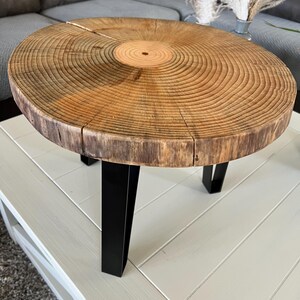 May include: A round wooden coffee table with a natural wood finish and black metal legs. The table top is a cross-section of a tree trunk, showing the rings.