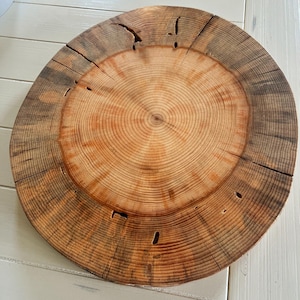 May include: A round wooden serving tray with a natural wood finish. The tray has a circular design with concentric rings and a dark brown outer edge.