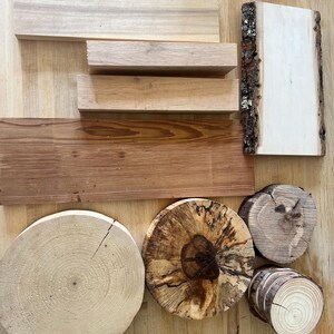 May include: Assortment of natural wood pieces, including rectangular planks and circular cross-sections. The wood varies in color from light beige to dark brown, with visible grain patterns and bark edges. Ideal for craft projects.