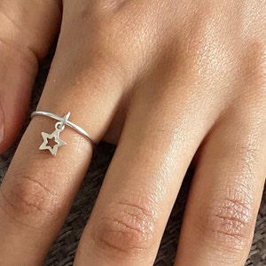 May include: A silver ring with a dangling star charm. The ring is thin and delicate, and the star is openwork.