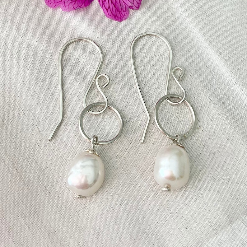 Handmade sterling silver and pearl earrings. The freshwater pearls on these earring measure approximately 10mm. The pearls are threaded onto a sterling silver wire and dangling on a 10mm hoop. The sterling silver ear wire are attached to the hoop