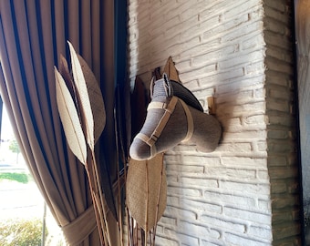 May include: A brown and gray horse head wall decor with a black and white patterned hat. The horse head is mounted on a white brick wall.