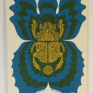 Puede incluir: Un cartel de concierto vintage con un gráfico de mariposa estilizado en azul, verde y amarillo. El cartel anuncia un concierto con Staple Island, Singer Kirk y Lysa Holley. El texto "Bill Graham Presents in San Francisco" aparece en la parte superior del cartel.