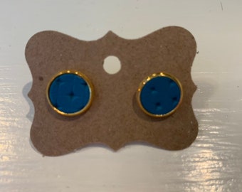 Peut inclure: Une paire de petites boucles d'oreilles rondes avec un bord doré et un centre bleu. Les boucles d'oreilles ont un motif texturé.