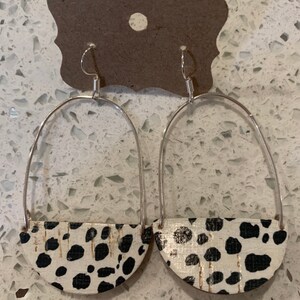 May include: A pair of silver hoop earrings with a black and white dalmatian print half-circle pendant.