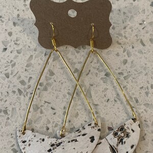 May include: A pair of gold hoop earrings with white and black ceramic crescent moon shapes hanging from them.