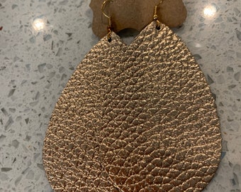 May include: A pair of gold-coloured teardrop earrings with a textured surface. The earrings are hanging from gold-coloured ear wires and attached to a brown cardboard tag.