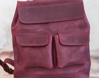 May include: A burgundy leather backpack with a flap closure and two front pockets. The bag has adjustable shoulder straps and a top handle. The leather has a slightly distressed appearance.
