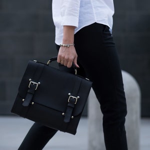 May include: A black leather satchel bag with silver buckles and metal accents. The bag has a flap closure and a top handle.