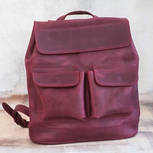 May include: A burgundy leather backpack with two large front pockets. The backpack has a flap closure and a top handle.