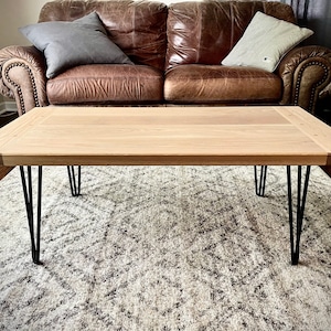 May include: A light wood coffee table with a rectangular top and black hairpin legs. The table is sitting on a patterned rug.