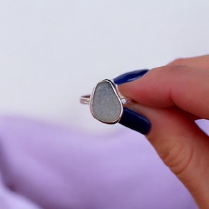 May include: A silver ring with a light grey sea glass stone set in the centre.