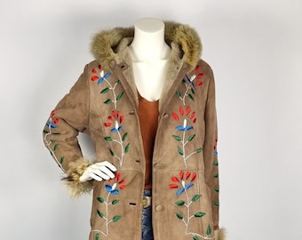 Könnte beinhalten: Eine braune Wildlederjacke mit einer Kapuze und Ärmelbündchen aus Kunstpelz. Die Jacke ist mit bunten Blumen und Ranken bestickt.