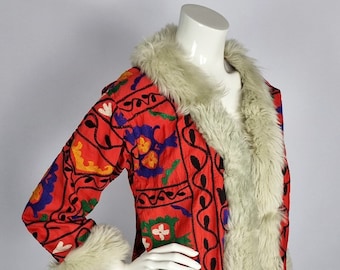 Puede incluir: Un abrigo rojo con intrincados bordados florales en amarillo, azul y verde. El abrigo presenta un cuello y puños de piel sintética color crema. El abrigo se exhibe en un maniquí.