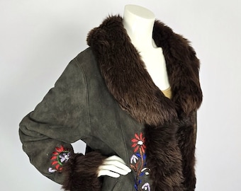 May include: A dark olive green suede coat with a brown fur collar and trim. The coat features colourful floral embroidery on the sleeves and front. The coat is displayed on a mannequin.