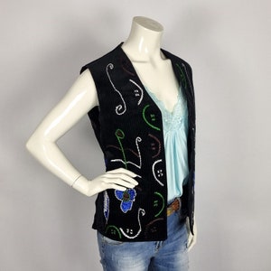 May include: A black sleeveless vest with colorful embroidered floral designs. The vest has a V-neck and is made of a textured fabric.