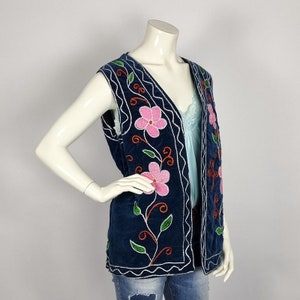 May include: A navy blue velvet vest with embroidered pink flowers and green leaves. The vest has a V-neck and a scalloped hem.