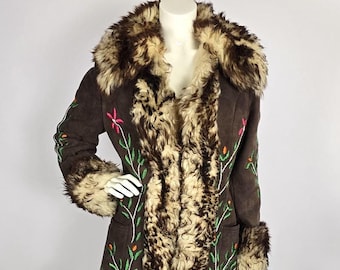Könnte beinhalten: Ein brauner Wildleder- und Schaffellmantel mit einem Pelzkragen und -ärmelaufschlägen. Der Mantel ist mit grünen Ranken und rosa Blumen bestickt.