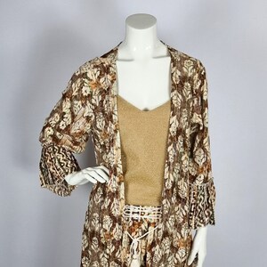 Peut inclure: Un kimono à imprimé floral brun et blanc avec des manches longues et un ourlet à volants. Le kimono est fait d'un tissu transparent et a une coupe ample.